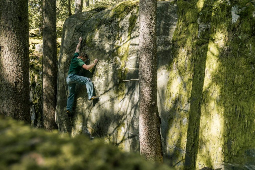 Das Bild zeigt einen Kletterer beim Bouldern im Maltatal, er klettert zwischen Bäumen einen hohen, plattigen Boulder