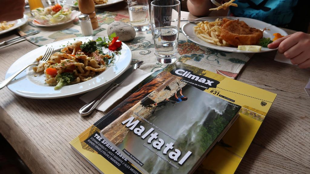 Das Bild zeigt einen gedeckten Tisch mit einem Spätzle Teller und dem Maltatal Kletterführer.