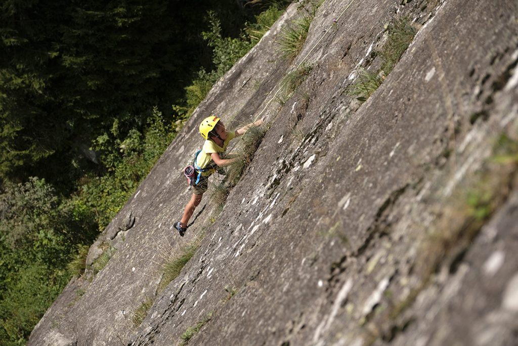 DAs Bild zeigt einen der Klettergärten im Mölltal, den Klettergarten Innerfragant. Ein kleiner Junge klettert in einer Granitplatte mit gelbem Shirt und Helm.