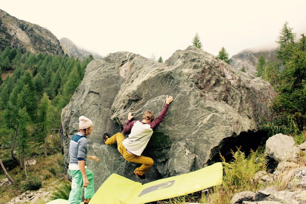 Das Bild zeigt einen Kletterer beim Obergailer Boulderfestival. Er klettert auf einem kleinen, grauen Felsblock und wird von einem Partner gespottet.