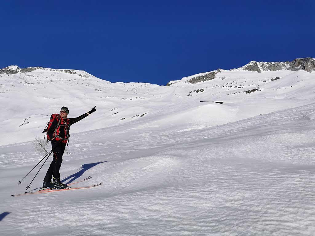 Das Bild zeigt den Aufstieg bei der Skitour Hochalmspitze über die Gössrinne. Ein Skitourengeher steht in verschneiter Hochgebirgslandschaft und zeigt mit dem Armbergauf.