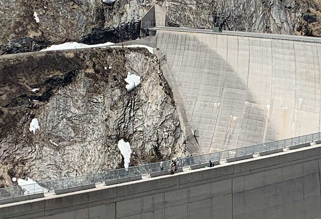 Das Bild zeigt Skitourengeher am Rückweg von der Skitour Oberlercherspitze. Sie gehen über die Krone des Kölnbreinsperre Staudamms. Man sieht die geschwungene Form der Sperre und die Felsen am südlichen Ende.